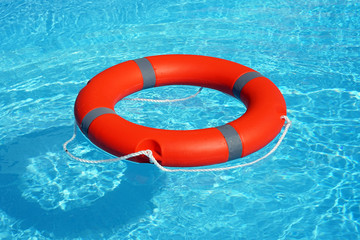 Orange lifebuoy pool ring float on blue water. Life ring floating on top of sunny blue water. Life ring in swimming pool   