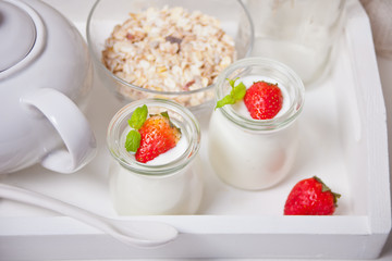 Two portions natural homemade yogurt in a glass jar with fresh strawberry and muesli nearby