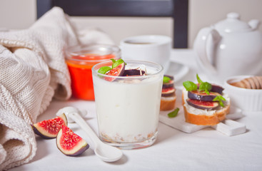 Yogurt with muesli and fig fruit in a glass, sandwich with cream cheese, figs and honey on the white treay. Healthy food concept.