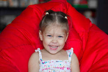 Portrait of laughing little girl sitting on red armchair