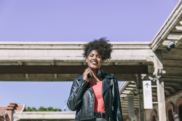 Beautiful girl with afro hair wearing casual clothes and black headphones around her neck, smiles looking at the camera on a sunny day