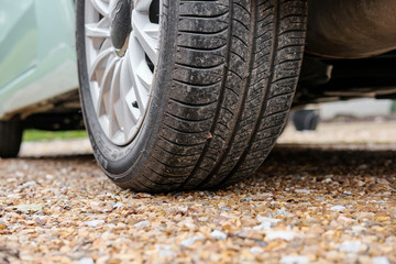 Ground level view of a new car, showing the rear tyre and tread together with the alloy wheel. Parked on a gravel driveway and showing some of its light blue paint.