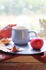Cup of coffee on the background of the window, behind which rain, apples, a warm scarf, leaves, autumn season, the concept of home comfort