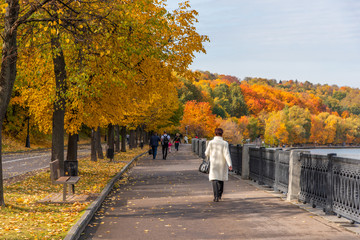 A woman in a white coat walks along the autumn promenade