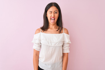 Beautiful chinese woman wearing white t-shirt standing over isolated pink background sticking tongue out happy with funny expression. Emotion concept.