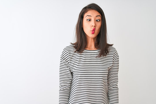 Young beautiful chinese woman wearing striped t-shirt standing over isolated white background making fish face with lips, crazy and comical gesture. Funny expression.