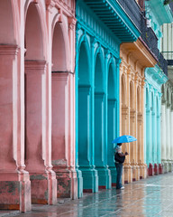 Multi colored colonial buildings main street Havana Cuba with a man in the rain with an umbrella