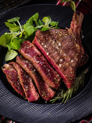 Steak on the bone. Rib eye. Tomahawk steak on the black plate with rosemary. Roasting - Rare....