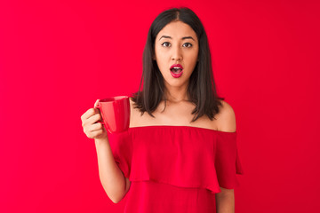 Young beautiful chinese woman drinking cup of coffee standing over isolated red background scared in shock with a surprise face, afraid and excited with fear expression