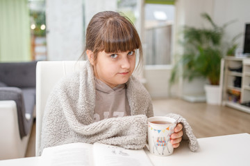 Young girl wrapping in plaid drinking thee at home, cold winter, reading book