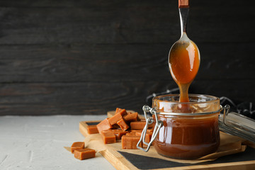 Glass jar with salted caramel and candies on grey background, space for text