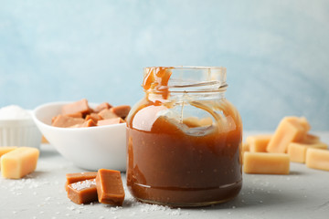 Glass jar with salted caramel and candies on grey background, space for text