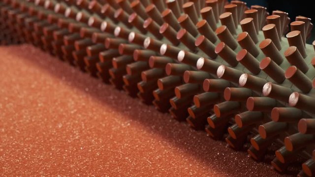 In production workshop for processing synthetic materials, orthopedic mattress production machine rotates with twisted rolls, pulls red sheet of paralon into its mechanism, desired relief of paralon