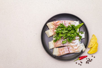 Raw pollock (Pollachius virens) pieces. Fresh fish for healthy food lifestyle. Lemon, parsley, sea salt, chili, black peppercorn
