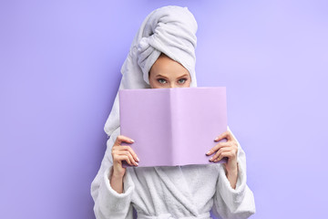 closed half of face of caucasian woman wearing bathrobe and towel after shower reading book isolated over purple background. Emotions, reading