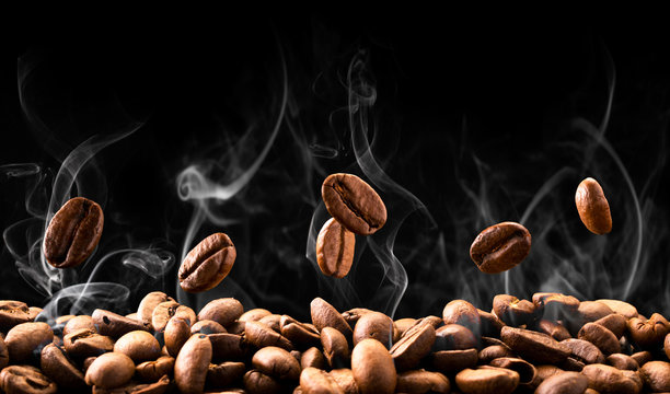 Coffee Beans Fall In Smoke On A Black Background. Roasting Coffee