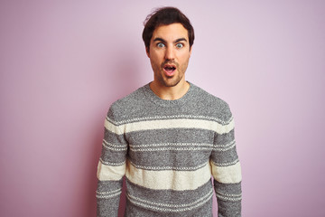 Fototapeta premium Young handsome man wearing casual striped sweater standing over isolated pink background afraid and shocked with surprise expression, fear and excited face.