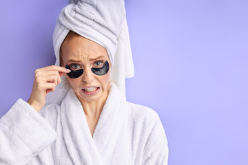 Caucasian female in bathrobe and towel removing patches from eye. Cosmetology and skin care concept.