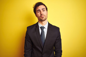 Young handsome businessman wearing suit and tie standing over isolated yellow background looking sleepy and tired, exhausted for fatigue and hangover, lazy eyes in the morning.