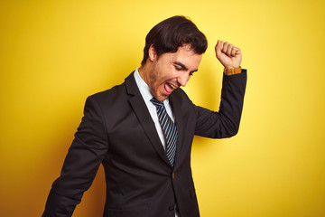 Young handsome businessman wearing suit and tie standing over isolated yellow background Dancing happy and cheerful, smiling moving casual and confident listening to music
