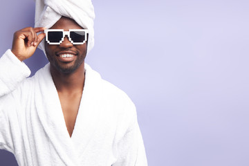 Young man in white bathrobe and towel look at camera smiling. Studio portrait against purple...