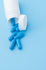 Blue capsules, pills on a blue background. Capsules in a white jar. Vitamins, nutritional supplements for women's health