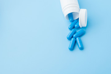 Blue capsules, pills on a blue background. Capsules in a white jar. Vitamins, nutritional supplements for women's health