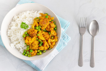 Rice and Cauliflower Curry with Green Peas in a Bowl Garnished with Cilantro Top View Photo on White Background.