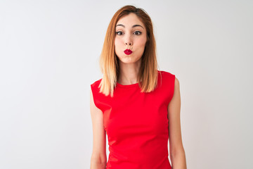 Redhead businesswoman wearing elegant red dress standing over isolated white background puffing cheeks with funny face. Mouth inflated with air, crazy expression.