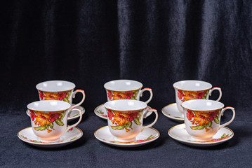 Set of cups and saucers for tea and coffee on a dark black fabric background
