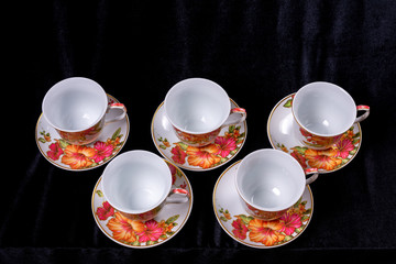 Set of cups and saucers for tea and coffee on a dark black fabric background