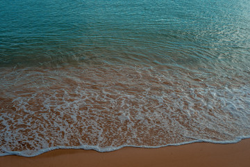 Waves crashing on the sand at the seashore with blue sea