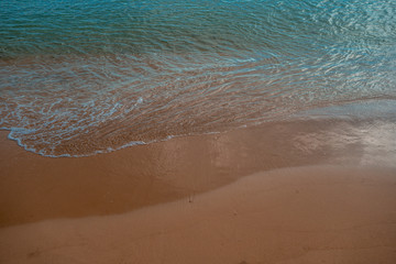 Fototapeta na wymiar Waves crashing on the sand at the seashore with blue sea
