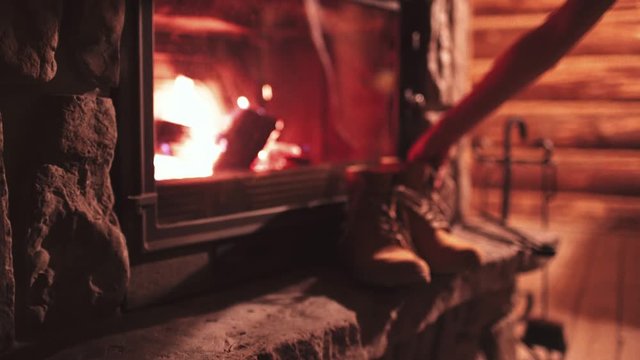 Woman Hand puts Winter Boots on a Shelf near Fireplace to get Warm. 4K. Vintage folk boots near the Cozy Fireside. Shoes getting dry near the burning fire at home, in chalet. Autumn and Winter Concept