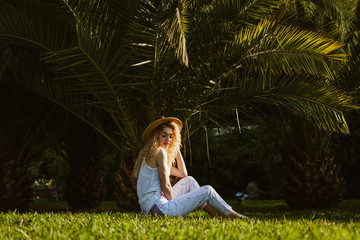 resting girl in the park sits on the grass on a background of palm trees