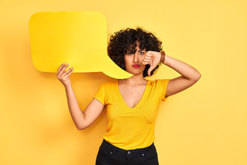 Young arab woman with curly hair holding speech bubble over isolated yellow background with angry...