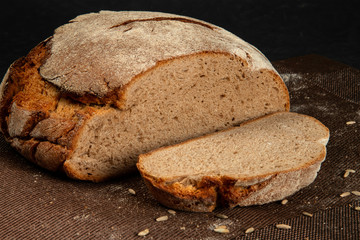close-up of a black loaf of bread with seeds on a dark napkin and a black background