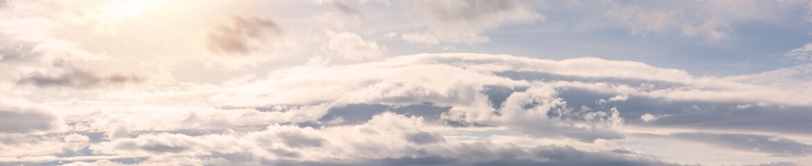 Obraz premium Beautiful summer sky background with warm sunny tonings. Sunny dawn over above clouds. Cloudscape. Natural background. Ultra wide panorama, banner format