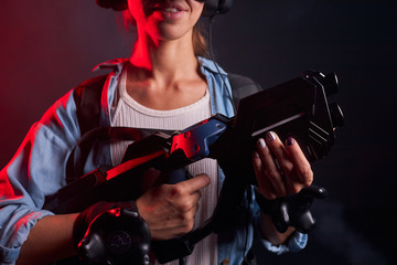 Cropped photo of young woman playing with VR weapon, speacial mask on head. Ultra violet