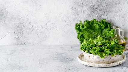 Green kale leaves in white craft bowl on gray cement background. Healthy eating, vegetarian food, dieting concept. Copy space left. Health kale benefits. Banner - obrazy, fototapety, plakaty