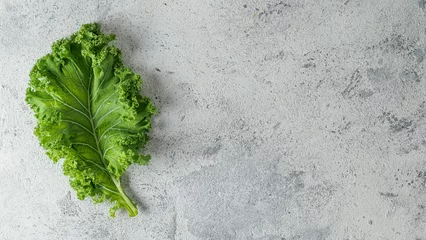 Poster Fresh green kale leaf on gray cement background, copy space for text or design. Flat lay or top view. Healthy detox vegetables. Clean eating and dieting concept. Health kale benefits © fascinadora