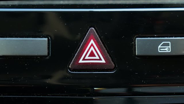 Emergency triangle on the dashboard of a vehicle, and a mana pressing the button, flashing red