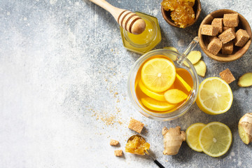 Hot cup of ginger tea and ingredients - lemon, ginger, honeycomb, honey on a gray stone countertop....