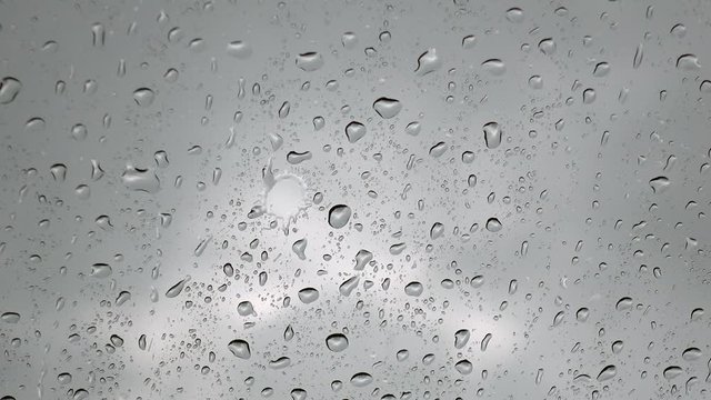 Close up view of water drops falling on glass. Rain running down on window. Rainy season, autumn. Raindrops trickle down, grey sky background