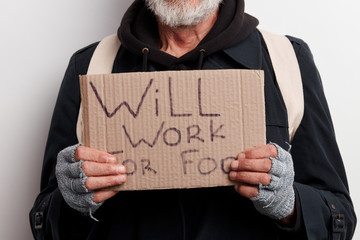 Unrecognizable homeless man holding sign, request for job, seeking help posing at studio over white...