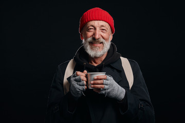 Bearded beggar male smiling, happy even living in street. Cheerful homeless man with mug of hot tea...