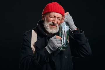 Old man with grey beard hugging empty bottle of alcohol. Male dressed in old street clothes...