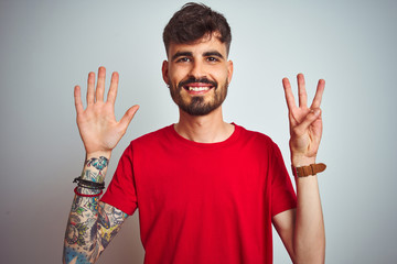 Fototapeta premium Young man with tattoo wearing red t-shirt standing over isolated white background showing and pointing up with fingers number eight while smiling confident and happy.