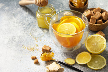 Hot cup of ginger tea and ingredients - lemon, ginger, honeycomb, honey on a gray stone countertop. Free space for your text.