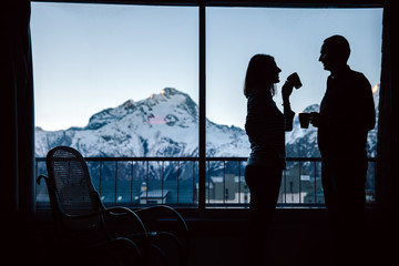Happy couple drinking morning coffe in a cozy home with a mountain view.